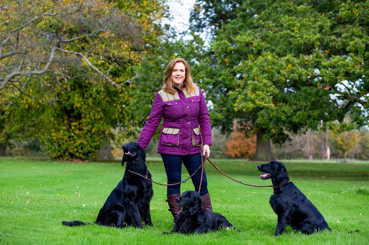 Jenny Campbell with 3 Flatcoated Retrievers on grass field